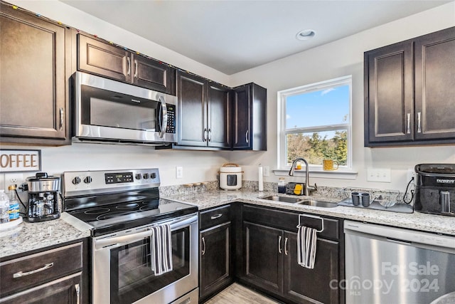 kitchen featuring appliances with stainless steel finishes, light stone counters, dark brown cabinets, and sink