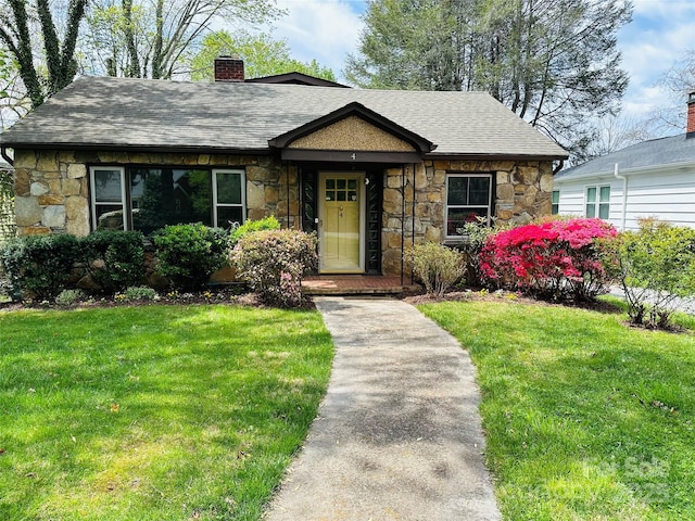 view of front facade featuring stone siding, a chimney, a front lawn, and a shingled roof