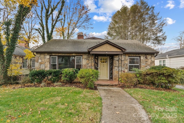 single story home with stone siding, a chimney, a front yard, and a shingled roof