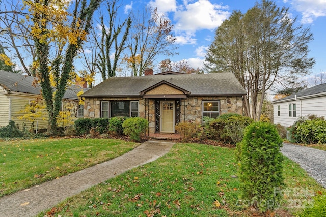 bungalow featuring stone siding, a front lawn, a chimney, and a shingled roof