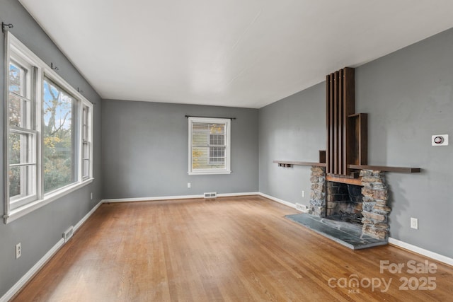 unfurnished living room with visible vents, a stone fireplace, baseboards, and wood finished floors