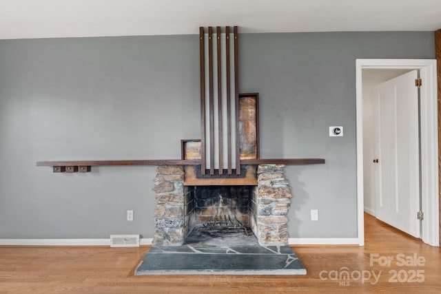 room details with visible vents, a fireplace, baseboards, and wood finished floors