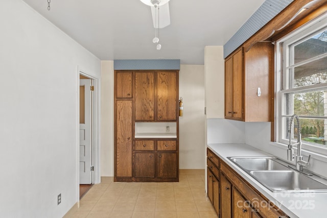 kitchen with light tile patterned floors, brown cabinetry, baseboards, a sink, and light countertops