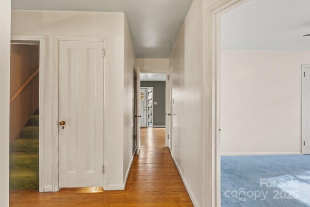 corridor with stairs, wood finished floors, and baseboards