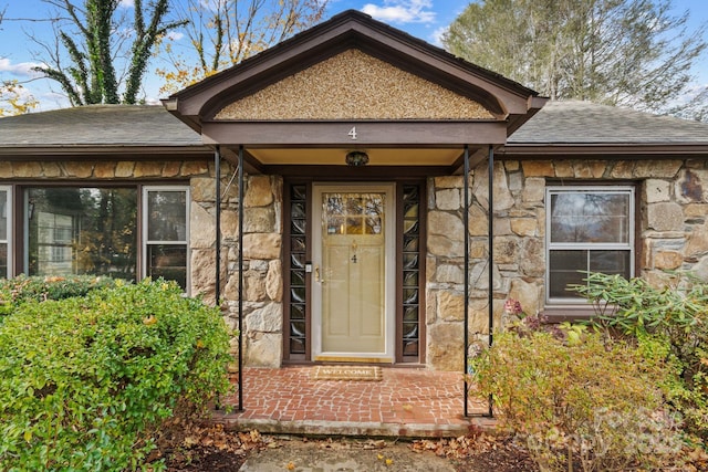 doorway to property featuring stone siding and a shingled roof