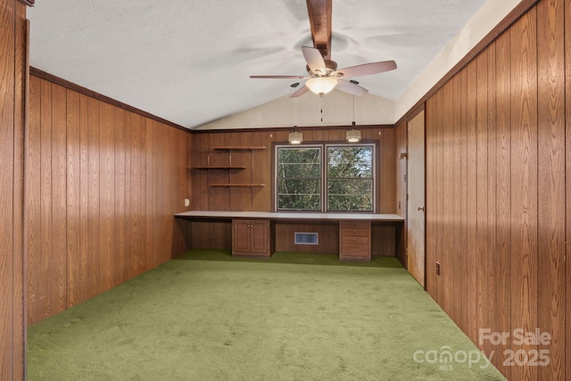 unfurnished office with a ceiling fan, carpet, visible vents, built in study area, and wood walls