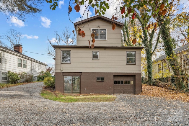 rear view of property with a garage, driveway, and stucco siding