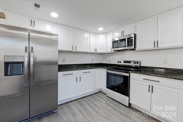 kitchen with white cabinets, appliances with stainless steel finishes, light hardwood / wood-style floors, and dark stone countertops