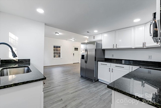 kitchen with sink, stainless steel appliances, light hardwood / wood-style flooring, dark stone counters, and white cabinets