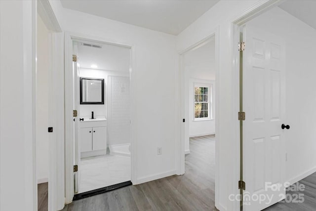 corridor with a sink, visible vents, baseboards, and wood finished floors