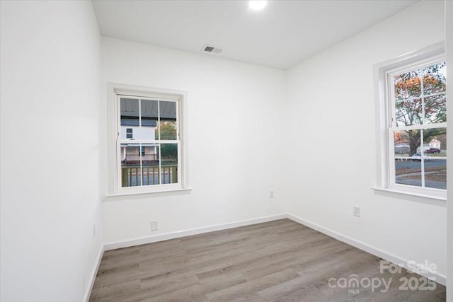 empty room featuring wood finished floors, visible vents, a wealth of natural light, and baseboards