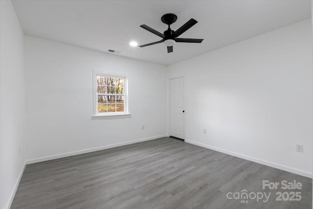 empty room featuring a ceiling fan, visible vents, wood finished floors, and baseboards