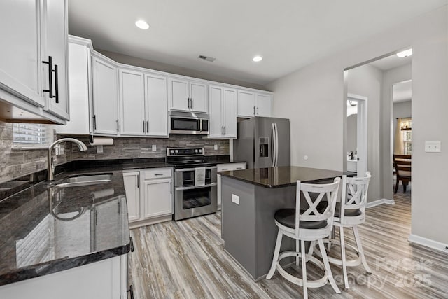 kitchen featuring stainless steel appliances, white cabinets, a kitchen island, and sink