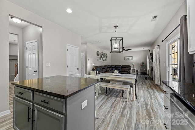 kitchen with decorative light fixtures, dark stone countertops, ceiling fan with notable chandelier, light hardwood / wood-style flooring, and a center island