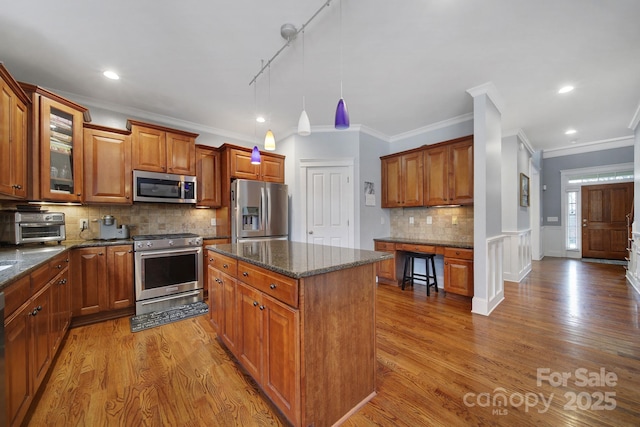 kitchen with pendant lighting, appliances with stainless steel finishes, a center island, light hardwood / wood-style floors, and dark stone counters