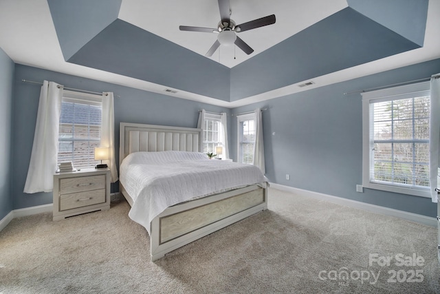 carpeted bedroom featuring ceiling fan, a tray ceiling, and multiple windows