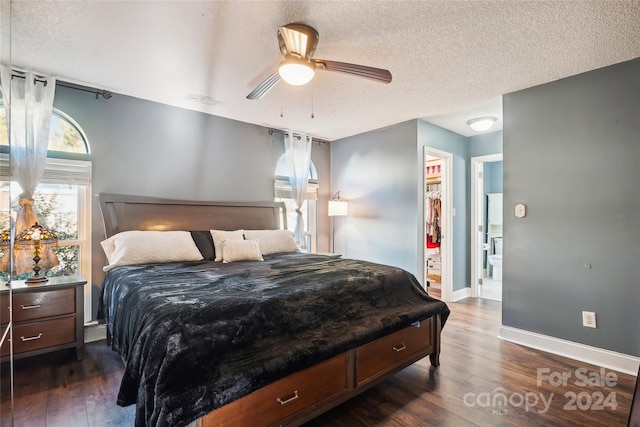 bedroom featuring dark wood-type flooring, a walk in closet, ceiling fan, a textured ceiling, and a closet