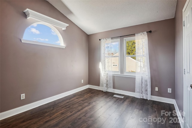 spare room with a textured ceiling, dark wood-type flooring, and vaulted ceiling