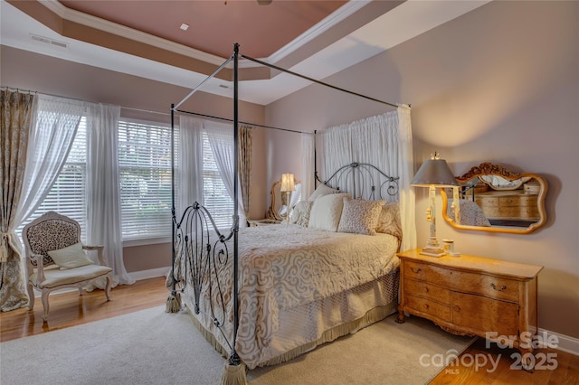 bedroom featuring baseboards, visible vents, a raised ceiling, ornamental molding, and wood finished floors