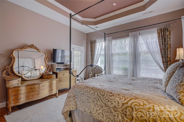 bedroom with a tray ceiling, wood finished floors, visible vents, and crown molding