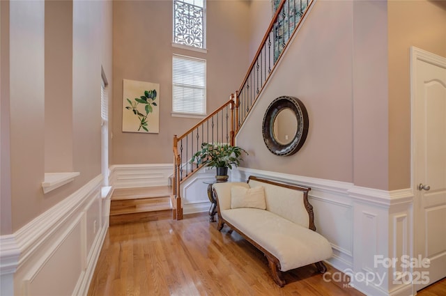 foyer entrance with light wood-style flooring, a decorative wall, a towering ceiling, and stairs