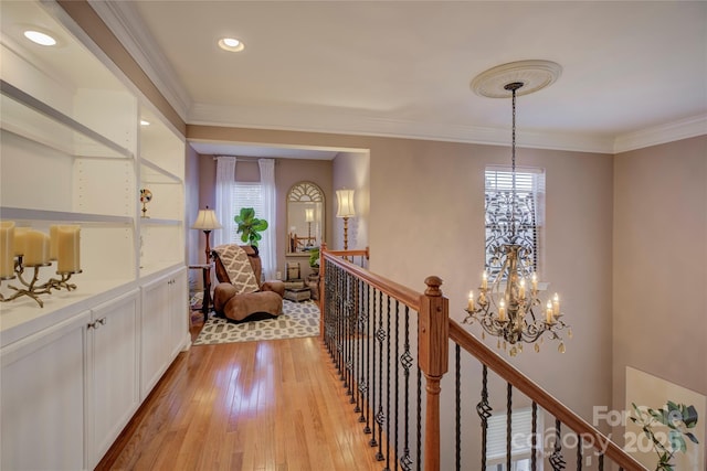 hallway featuring light wood-type flooring, a healthy amount of sunlight, ornamental molding, and a notable chandelier