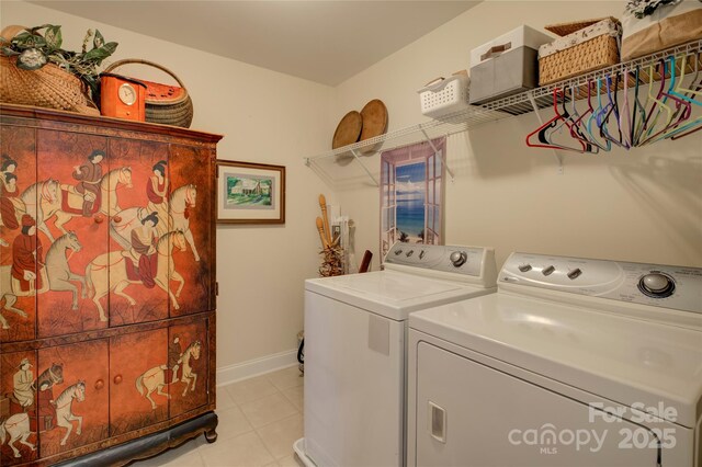 clothes washing area with laundry area, baseboards, washing machine and clothes dryer, and light tile patterned floors