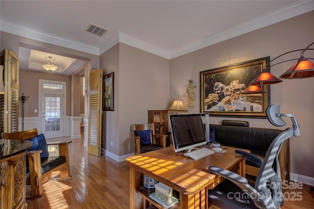 office area with a wainscoted wall, light wood finished floors, visible vents, and crown molding