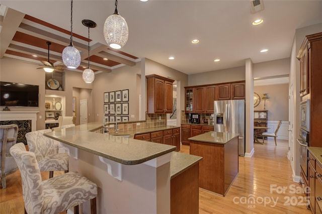 kitchen featuring pendant lighting, brown cabinets, stainless steel appliances, open floor plan, and a peninsula