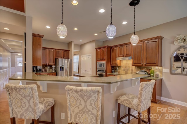 kitchen with stainless steel appliances, a breakfast bar, brown cabinetry, and a peninsula