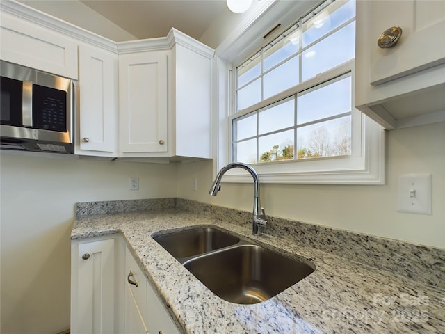 kitchen featuring white cabinets, light stone countertops, and sink