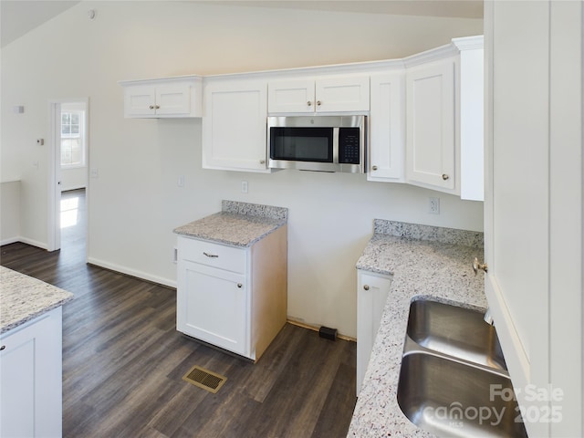 kitchen featuring light stone countertops, vaulted ceiling, dark wood-type flooring, sink, and white cabinets