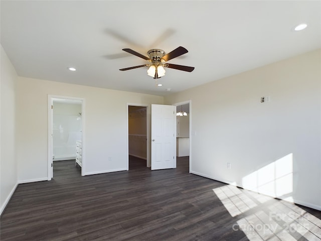 unfurnished bedroom featuring ensuite bath, a spacious closet, ceiling fan, dark wood-type flooring, and a closet