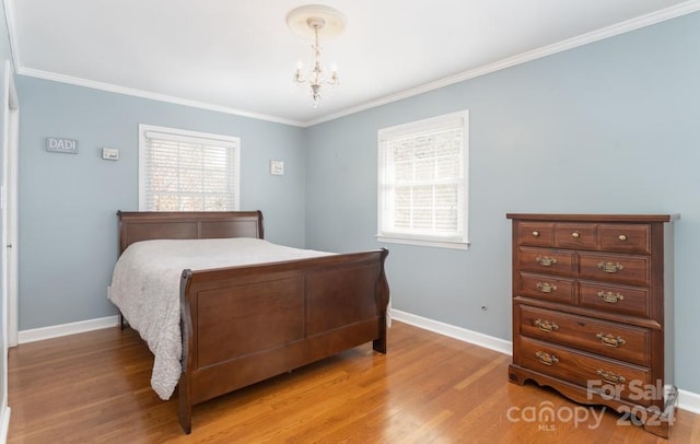 bedroom with wood-type flooring, ornamental molding, and an inviting chandelier