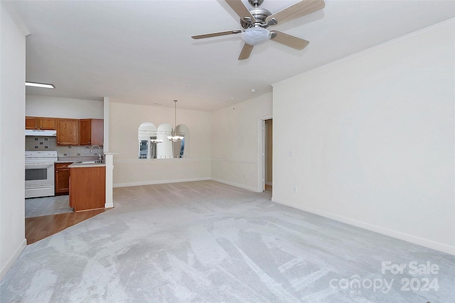 unfurnished living room featuring ceiling fan with notable chandelier, light colored carpet, ornamental molding, and sink