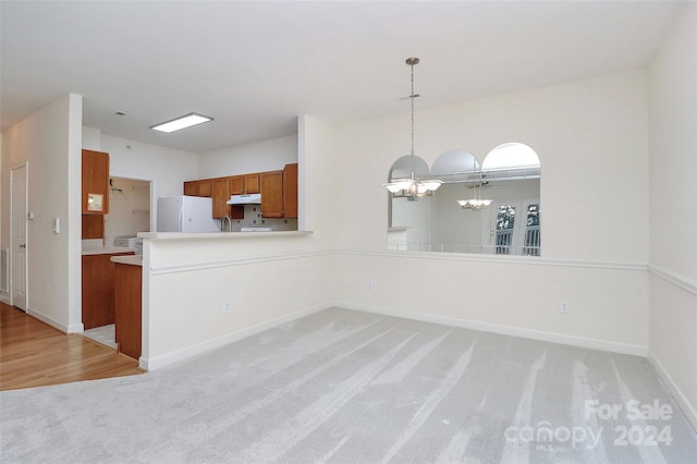 kitchen featuring kitchen peninsula, light colored carpet, decorative light fixtures, an inviting chandelier, and white fridge