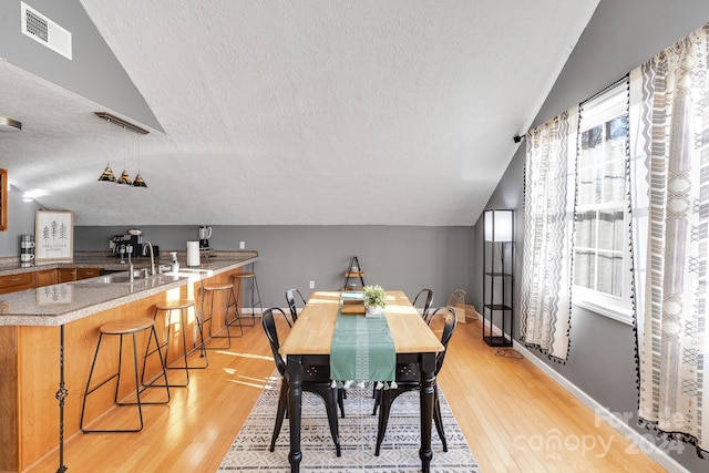 dining area with a textured ceiling, light hardwood / wood-style floors, a wealth of natural light, and sink