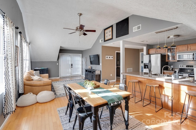 dining space with ceiling fan, sink, light hardwood / wood-style flooring, high vaulted ceiling, and a textured ceiling