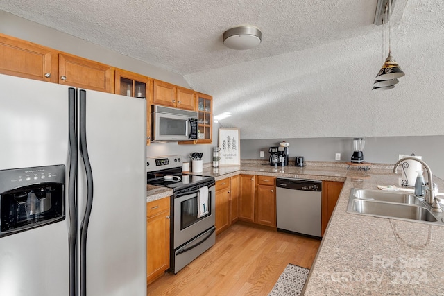 kitchen with appliances with stainless steel finishes, a textured ceiling, vaulted ceiling, sink, and light hardwood / wood-style floors