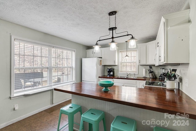 kitchen with white cabinets, a wealth of natural light, white fridge, and wood counters