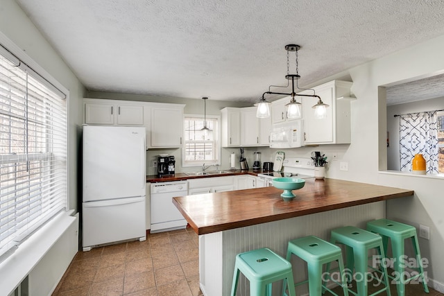 kitchen with wood counters, white appliances, decorative light fixtures, and a wealth of natural light