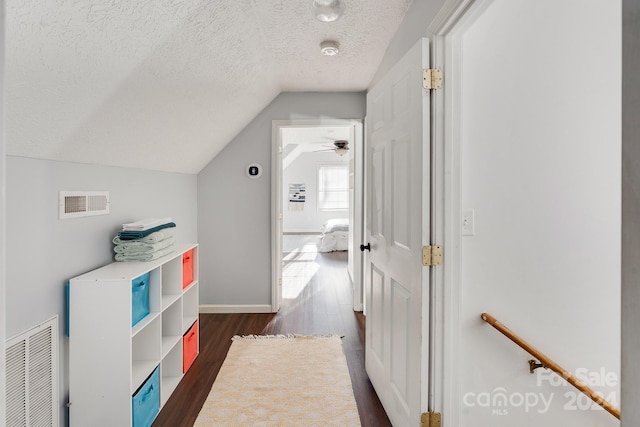 hallway with a textured ceiling, dark wood-type flooring, and vaulted ceiling