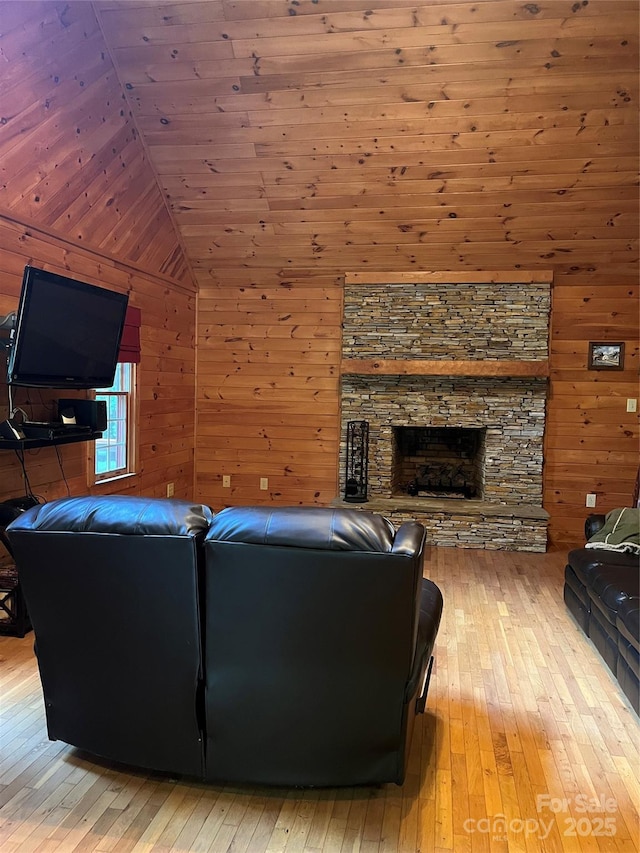 living room with a stone fireplace, light hardwood / wood-style flooring, and wood walls