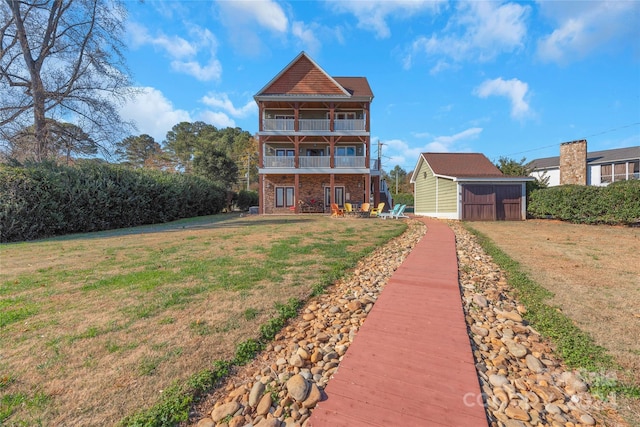 rear view of property featuring a lawn, a balcony, and an outbuilding