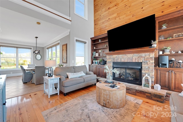 living room featuring a fireplace, a towering ceiling, light hardwood / wood-style floors, and ornamental molding