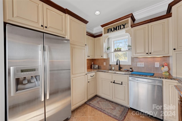 kitchen with cream cabinetry, sink, stainless steel appliances, and dark stone counters