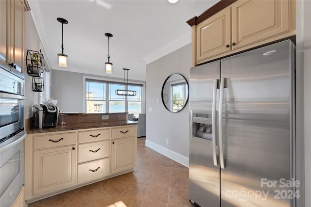 kitchen featuring pendant lighting, stainless steel appliances, dark stone counters, and cream cabinets