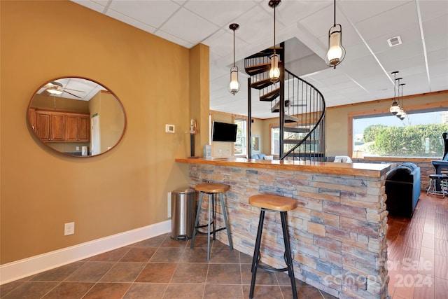 kitchen with a kitchen breakfast bar, dark hardwood / wood-style floors, kitchen peninsula, pendant lighting, and a paneled ceiling