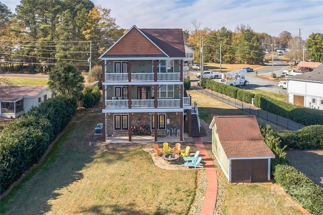 back of property with a yard, an outdoor fire pit, an outdoor structure, a balcony, and a patio