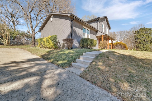 view of side of home featuring brick siding, a lawn, and fence